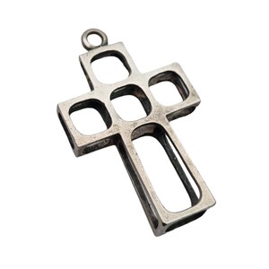 Könnte beinhalten: Ein silberner Kreuzanhänger mit geometrischem Design. Das Kreuz besteht aus mehreren Quadraten, die miteinander verbunden sind.