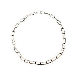 Può includere: Una collana a catena color argento con maglie rettangolari allungate. Ogni maglia è collegata da una barra orizzontale centrale, creando un motivo uniforme lungo tutta la lunghezza della catena. La collana include una piccola chiusura in metallo.