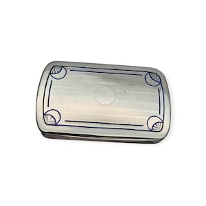 May include: A rectangular silver-toned box with rounded corners. The lid features a linear pattern and a dark blue border with decorative corner designs. A small circular detail is in the center of the lid.