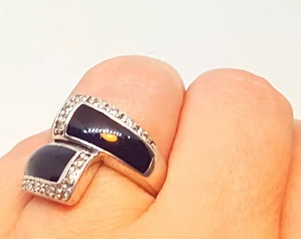 May include: A silver ring with black enamel and small clear stones. The ring is designed in a modern style with a unique shape.