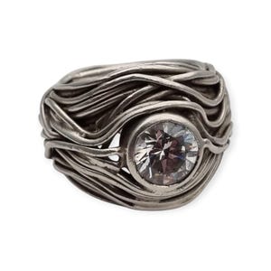 May include: A silver ring with a large, clear, round gemstone set in a woven band.