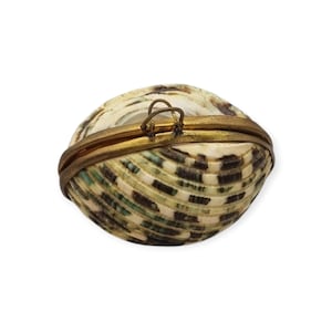 May include: A small, oval-shaped hinged box crafted from a natural seashell with a cream, brown, and green mottled pattern. The container features a metallic gold-toned brass rim and a small, circular metal loop attached to the top edge.