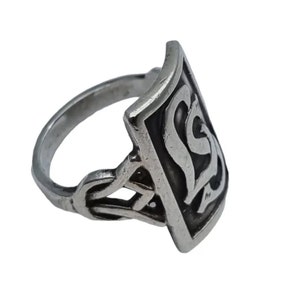 Può includere: Un anello d'argento con un design rettangolare che presenta una lettera 'S' stilizzata al centro. La fascia dell'anello è finemente progettata con un motivo a nodo celtico.