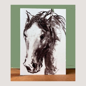 Puede incluir: Un dibujo en carboncillo blanco y negro de la cabeza de un caballo. El caballo está mirando hacia la izquierda y su crin ondea al viento.