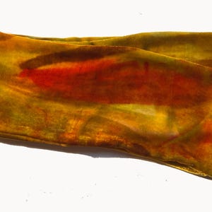 May include: A handmade textile scarf in shades of yellow, orange, and red. The scarf has a velvet-like texture and a rectangular shape. A small black label with white text reads "DIANA HAND Handmade Textiles."