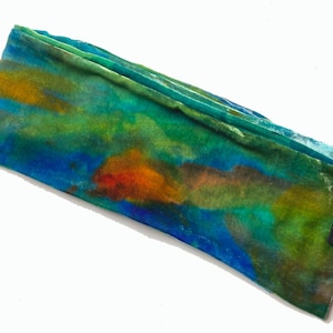 May include: A hand-dyed velvet scarf in shades of blue, green, orange, and yellow. The scarf is folded and has a label that reads "DIANA HAND Handmade Textiles."