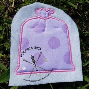 Può includere: Applique viola e rosa di un sacchetto della spazzatura con pois bianchi. L'applique è circondato da un punto di raso rosa. L'applique è su uno sfondo bianco con il testo "Rocking a Stitch" e "Quality Applique and Embroidery Design".