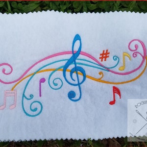 May include: Colorful embroidered design featuring a treble clef, musical notes, and a sharp symbol. The design is on a white fabric background.