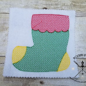 Może przedstawiać: Zielona, czerwona i żółta haftowana choinkowa skarpetka z falbanką na górze. Skarpetka znajduje się na białym tle.