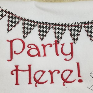 Peut inclure: Tissu blanc avec du texte brodé en rouge qui dit "Party Here!" et une guirlande en tissu à motifs noir et blanc au-dessus du texte.
