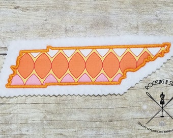 May include: An orange, pink, and yellow patterned applique of the state of Tennessee. The applique is outlined in orange thread and is on a white background. The text "Rocking a Stitch" is in the lower right corner of the image.