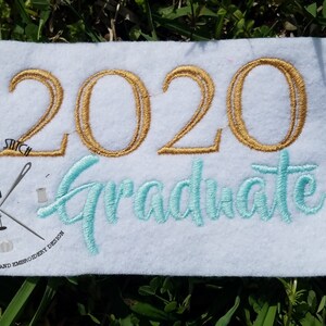 Puede incluir: Bordado dorado 2020 sobre una tela blanca con la palabra "Graduate" en letra cursiva turquesa. La esquina inferior izquierda tiene un pequeño logotipo con el texto "Rocking a Stitch" y "Quality Applique and Embroidery Design."