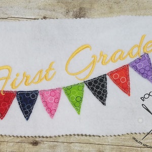 Peut inclure: Broderie représentant "Première année" avec un crayon et une guirlande de fanions colorés. Les fanions sont décorés de cercles blancs sur des fonds de couleurs variées. Le motif est sur un fond de feutre blanc.