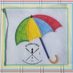Puede incluir: Aplicación de un paraguas colorido sobre un fondo blanco. El paraguas presenta paneles verdes con círculos blancos, amarillos, azules y rojos con círculos blancos. El mango es azul con un extremo curvo dorado. El texto "ROCKING A STITCH" está debajo.