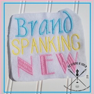 May include: Embroidered patch with the text "Brand Spanking New" in blue, yellow, and pink thread. The patch is on a white background and has a small logo in the bottom right corner that says "Rockin' a Stitch" with a sewing needle and thread design.