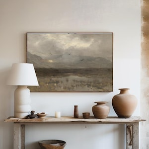 A styled hallway console with a large hanging painting featuring a dark and moody landscape painting of a marsh, the sun trying to come out from behind the clouds and birds flying overhead. Accessories the hallway table.