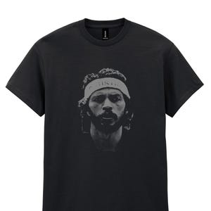 May include: Black t-shirt featuring a grayscale portrait of a person wearing a headband with the word "JUSTICE" printed on it. The portrait is centered on the shirt.