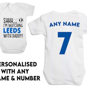 May include: White baby bodysuit with blue text that reads "SHHH... I'M WATCHING LEEDS WITH DADDY!" and a blue soccer ball graphic. A second white baby bodysuit with blue text that reads "ANY NAME" and the number "7" in blue.
