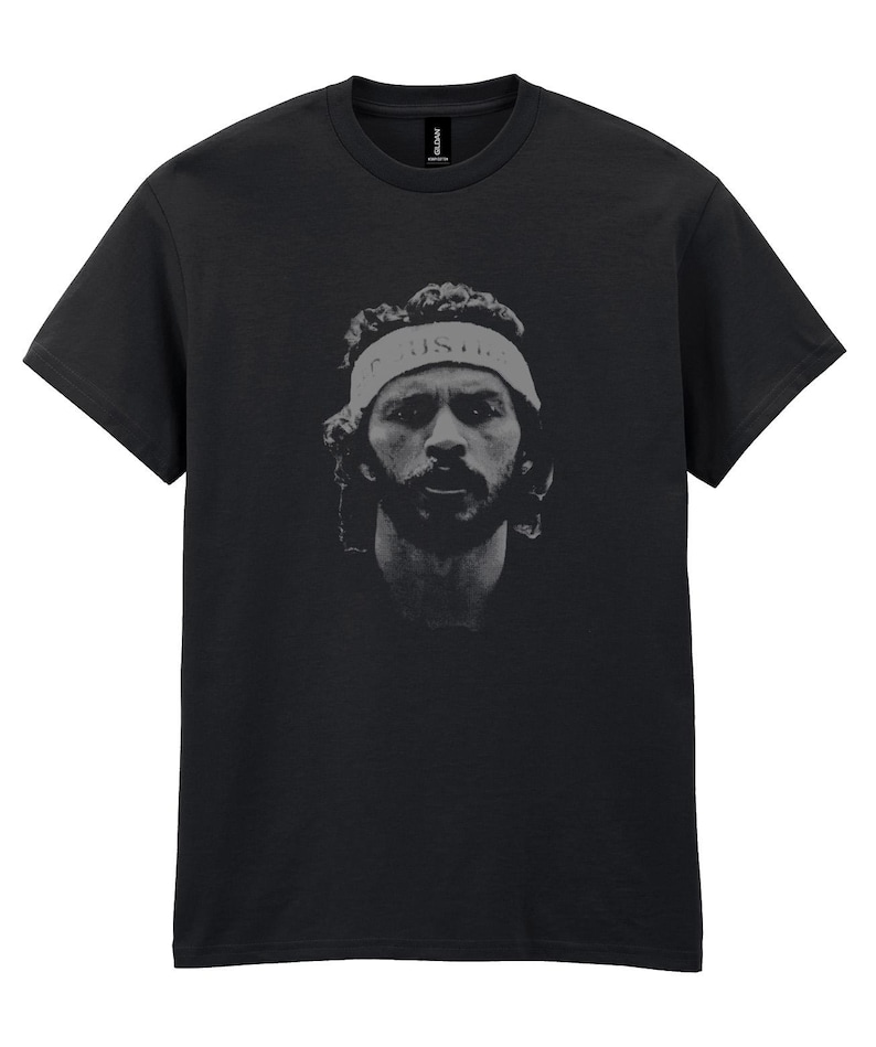 May include: Black t-shirt featuring a grayscale portrait of a person wearing a headband with the word "JUSTICE" printed on it. The portrait is centered on the shirt.