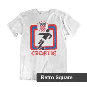 May include: White t-shirt with a red, blue, and white graphic of a soccer player kicking a ball inside a square with the word "CROATIA" underneath. The graphic has a retro style.