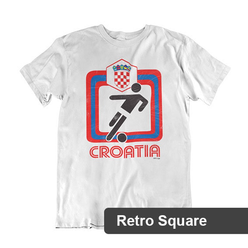 May include: White t-shirt with a red, blue, and white graphic of a soccer player kicking a ball inside a square with the word "CROATIA" underneath. The graphic has a retro style.