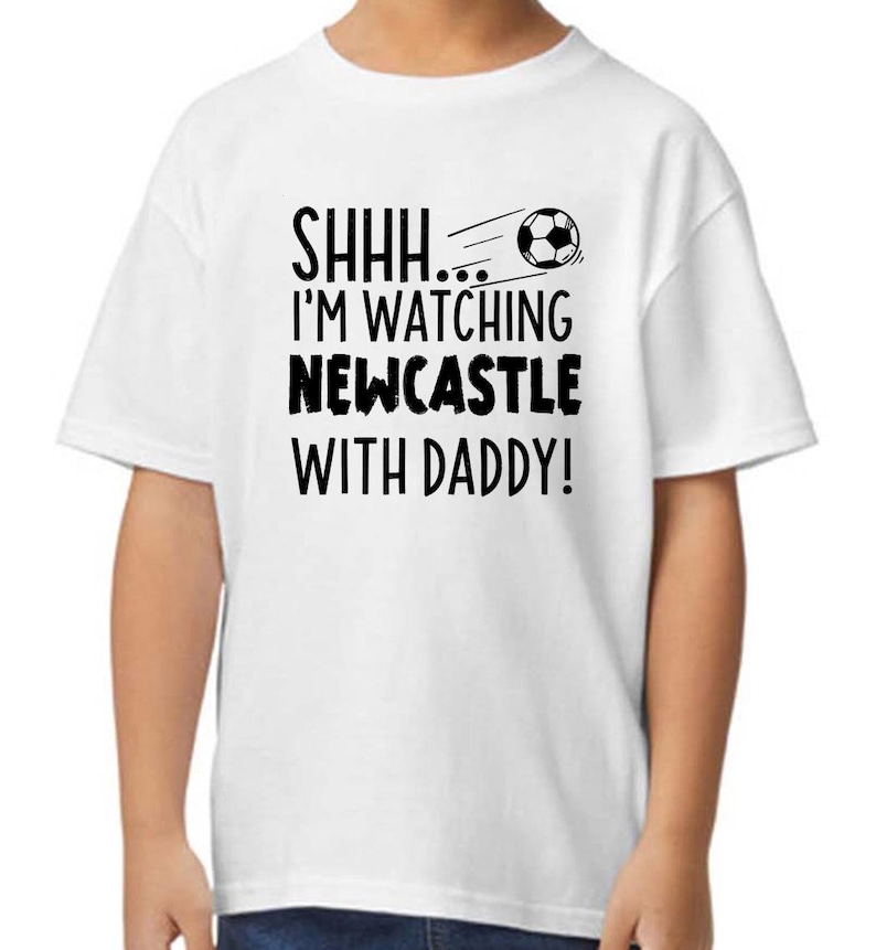 Peut inclure: T-shirt blanc avec du texte noir qui dit "SHHH... I'M WATCHING NEWCASTLE WITH DADDY!" et un graphique de ballon de football noir et blanc.