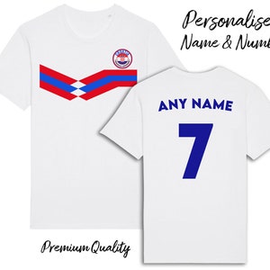 May include: White t-shirt with a blue and red chevron design and a Croatian national team logo on the front. The back of the shirt has "ANY NAME" and the number "7" printed in blue.