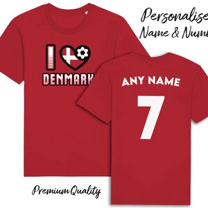 May include: Red t-shirt with a white "I love Denmark" graphic featuring a heart with the Danish flag and a football. The back of the shirt has "ANY NAME" and the number "7" in white.