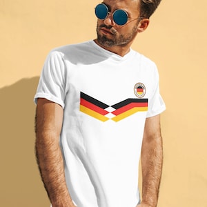 May include: White t-shirt featuring a black, yellow and red German flag design and a black circle with the word "Deutschland" and a small German flag inside.
