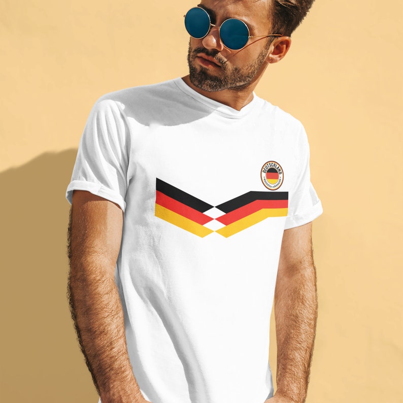 May include: White t-shirt featuring a black, yellow and red German flag design and a black circle with the word "Deutschland" and a small German flag inside.