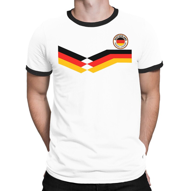 以下が含まれることがあります： 黒の襟元の白いTシャツで、前面にドイツ国旗のデザインが施されています。デザインは、黄色、赤、黒の旗で、その上に円の中に「DEUTSCHLAND」という文字が書かれています。