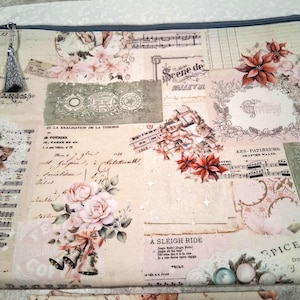 May include: A rectangular fabric pouch with a zipper closure and a silver tassel, featuring a vintage-style collage print with poinsettias, roses, musical notes, script text, and the words A SLEIGH RIDE, LES PATINEURS, and SCENE DE BALLET.