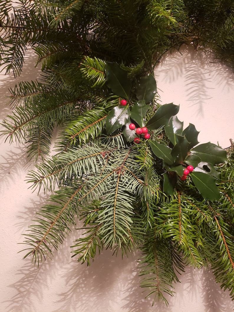 May include: A close-up of a Christmas wreath made with evergreen branches and holly sprigs with red berries.