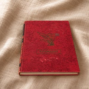 May include: A red book with the word "PSYCHOLOGY" printed on the cover. The cover features a textured pattern and a green illustration of a bird. The book's spine is black and gold.