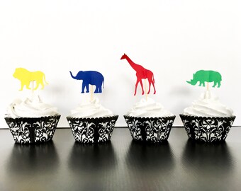 May include: Four cupcakes decorated with animal-shaped toppers. The cupcakes are in black and white patterned liners. The toppers are a yellow lion, a blue elephant, a red giraffe, and a green rhinoceros.