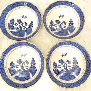 May include: Four matching blue and white porcelain bowls with a classic Willow pattern design. Each bowl features a scalloped edge, a gold rim, and a detailed landscape scene with trees, buildings, and flying birds. A timeless addition to any dining set.