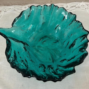 May include: A teal green glass bowl with a ruffled edge and a textured surface. The bowl is shaped like a leaf.