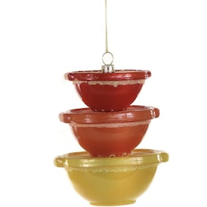 May include: A decorative Christmas ornament featuring three stacked mixing bowls in red, orange, and yellow. Each bowl has a glittery rim and is suspended by a gold string, creating a festive kitchen-themed decoration.