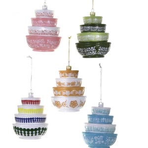 May include: A collection of hanging ornaments shaped like stacked mixing bowls. Each ornament features a different color and floral or patterned design. The ornaments are suspended by silver or gold cords, perfect for holiday decorating.
