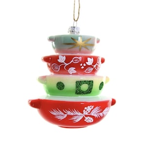 May include: A stacked ornament shaped like vintage mixing bowls. The top bowl is mint green with a gold starburst design. The middle bowls are red and green with white floral patterns. The ornament is suspended by a gold string.