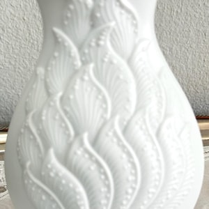 May include: A white porcelain vase with an embossed floral design. The vase has a round body and a narrow neck.