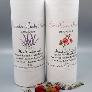 May include: Two white cylindrical containers of body powder, one labeled "Lavender Body Powder" and the other "Rose Body Powder." Each container has text and illustrations of lavender and roses. The containers are 6 oz each.