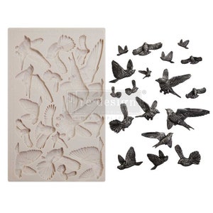 Puede incluir: Un molde de silicona con una variedad de diseños de pájaros en vuelo. El molde es de color blanquecino, con formas detalladas de pájaros. Junto al molde hay varios pájaros fundidos en color gris oscuro, mostrando el producto terminado.