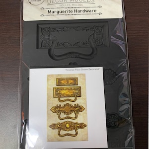 May include: A black silicone mold for making decorative hardware. The mold is 5 inches by 8 inches and features a design for a door handle and a rectangular plaque. The mold is food safe and oven safe up to 500 degrees Fahrenheit. The mold is also freezer safe to -100 degrees Fahrenheit.