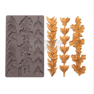 May include: A silicone mold with 8 different designs of oak leaf and berry garlands. The mold is gray and the garlands are shown in a golden color.