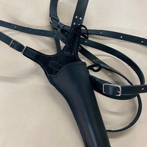 May include: Black leather holster with adjustable straps and a buckle closure. The holster is designed to be worn across the chest and shoulder. The leather is stitched and has a suede interior.