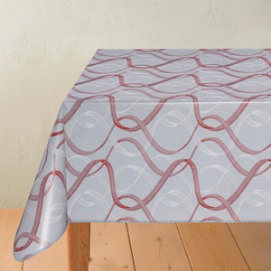 May include: A rectangular tablecloth featuring a pattern of red and white wavy lines on a light grey background. The cloth is draped over a table, displaying the design and texture. The table is made of wood.