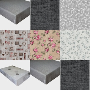 May include: A collection of nine rectangular tablecloths featuring various patterns including solid grey, black cross-hatch, white floral, wood-grain with hearts, pink roses on beige, grey leaf prints, and white fabric with grey circles.