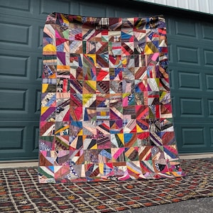 May include: A colorful patchwork quilt with a geometric design. The quilt features a variety of fabrics in shades of red, blue, yellow, and green. The quilt is displayed against a green garage door.
