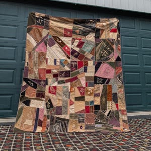 May include: A large rectangular quilt featuring a complex crazy quilt design composed of numerous irregular fabric patches in various colors including brown, pink, red, green, and cream, accented with decorative embroidery and stitching.